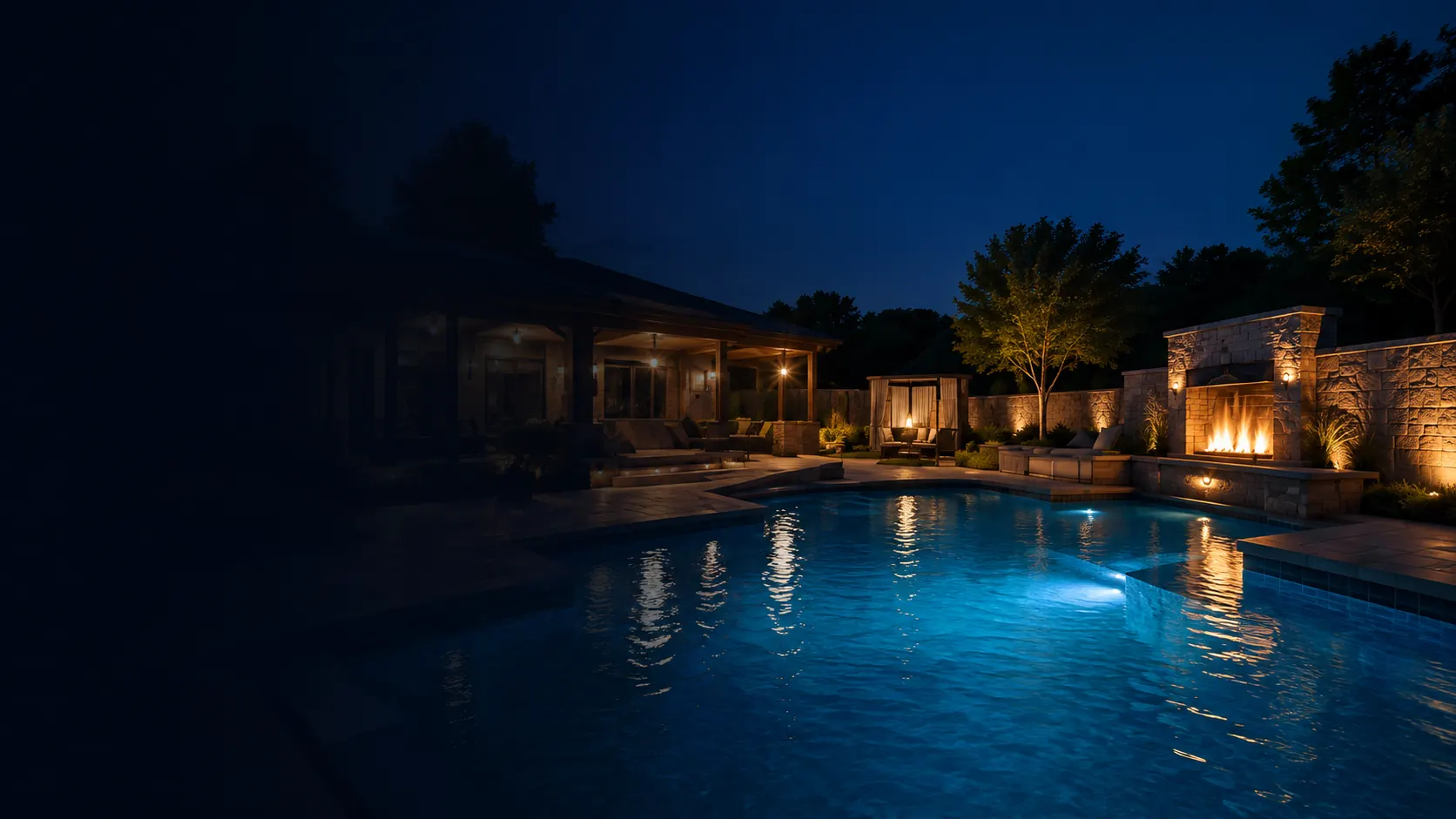 Backyard pool lit at night with fire features